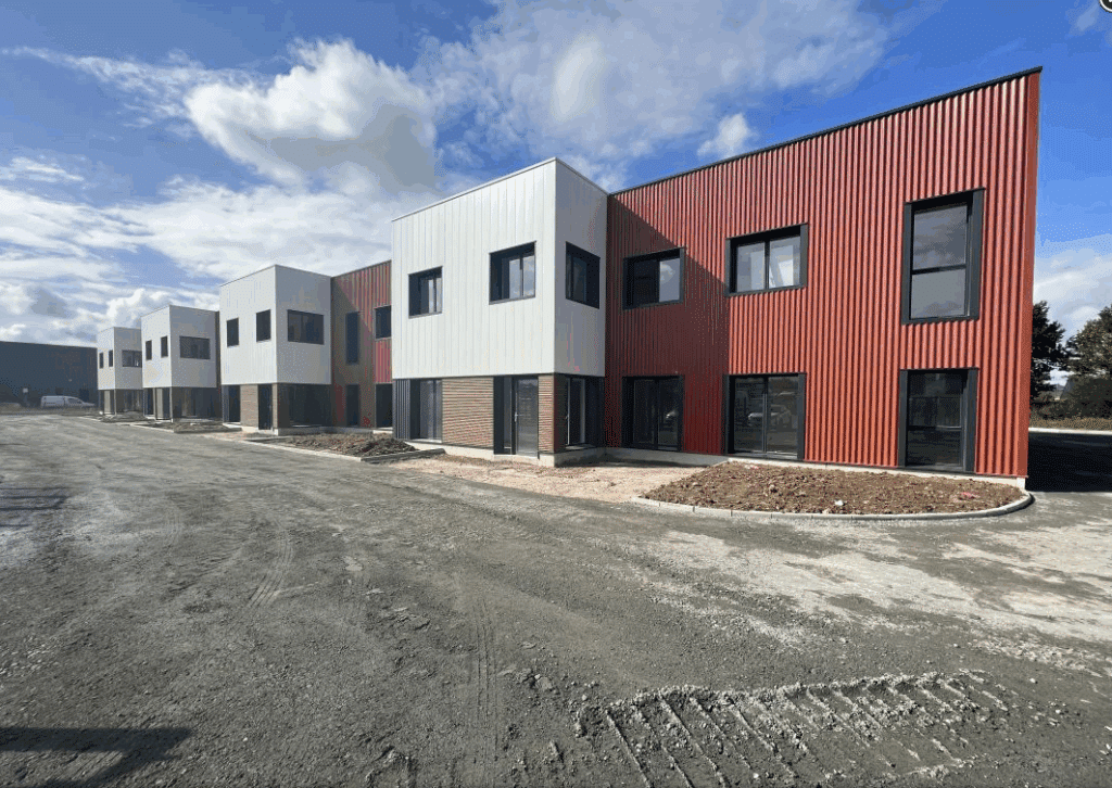 Ensemble de maisons neuves mitoyennes avec façades rouge brique et blanc, chantier de construction extérieur en gravier sous un ciel nuageux.