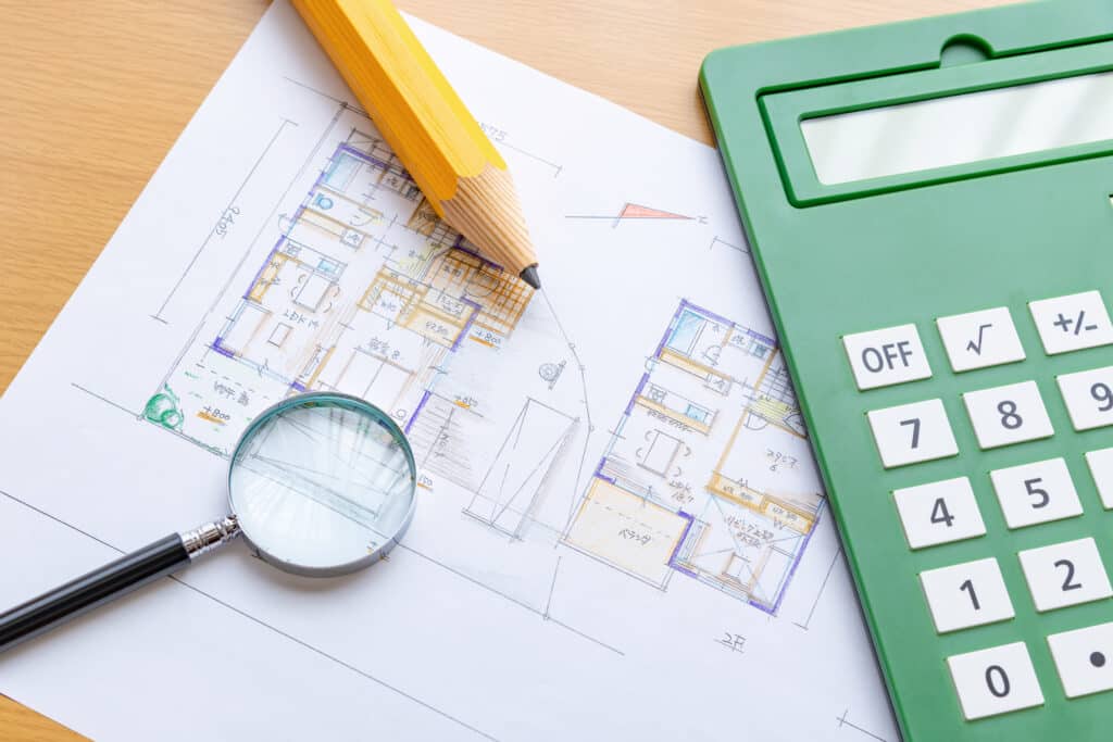 Plan d'Architecte et Calcul de Budget pour Construction Plan de maison détaillé avec grande calculatrice verte, loupe et crayon jaune pour l'estimation de coûts de construction.